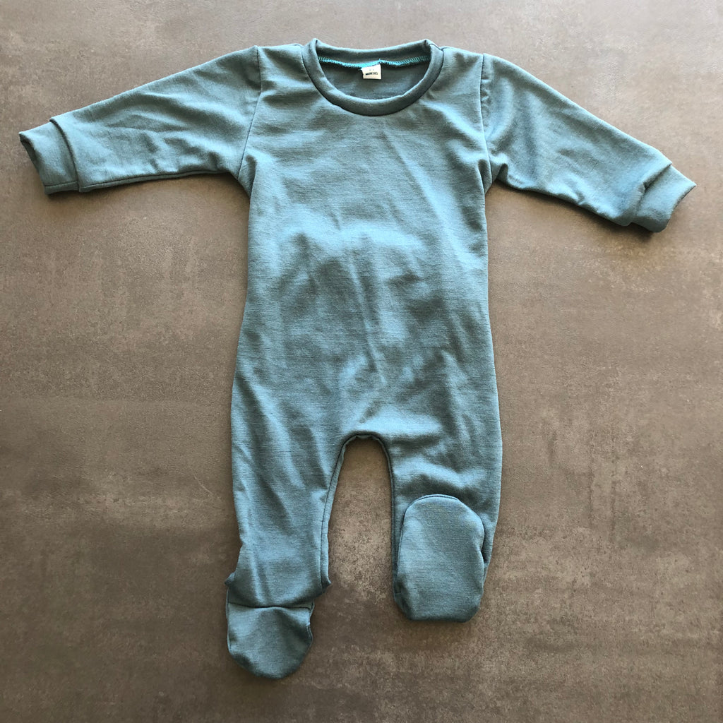 Flat lay of a baby grow in soft teal against a grey background