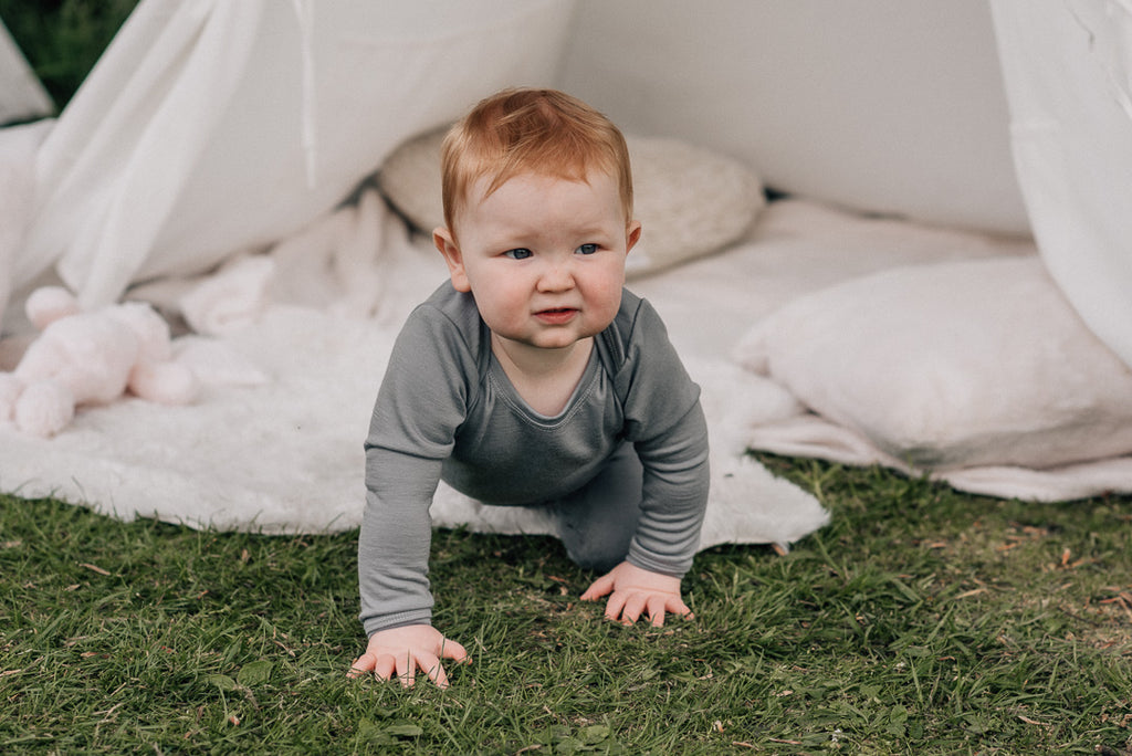 Toddler crawls towards the camera on the grass wearing merino pyjamas